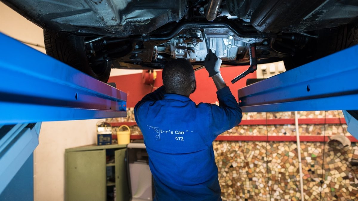 Stagiaire en formation mécanicien automobile travaillant sur une voiture positionnée sur un pont élévateur.
