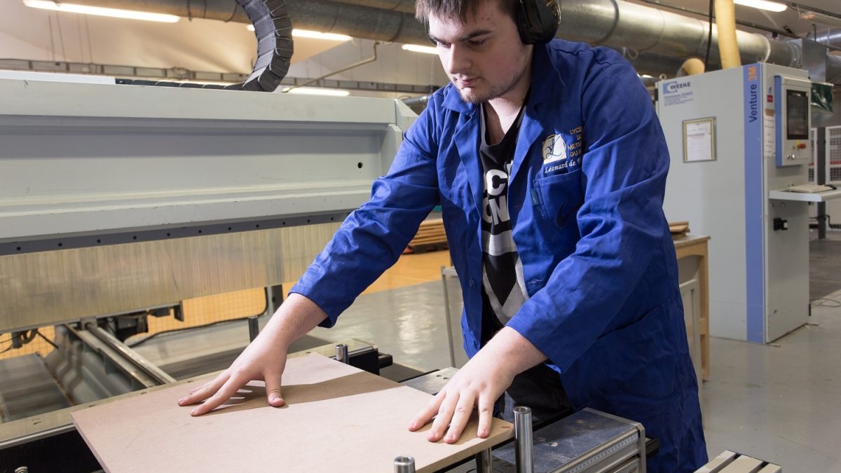 Stagiaire en formation pour adultes au Greta GPI2D utilisant une machine à commande numérique pour couper du bois dans le cadre de son CAP Menuisier Installateur.