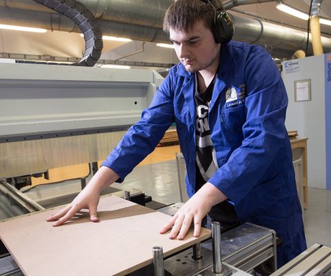 Stagiaire en formation pour adultes au Greta GPI2D utilisant une machine à commande numérique pour couper du bois dans le cadre de son CAP Menuisier Installateur.